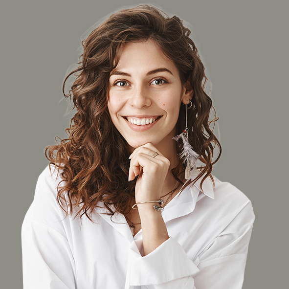 Cute happy european woman with curly hair in trendy white blouse, smiling broadly, leaning chin on hand, listening with interest to friend story, standing amused and joyful over gray wall. Emotions concept
